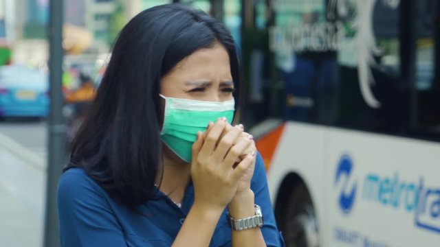 JAKARTA, Indonesia - April 24, 2019: Air Pollution Concept. Young woman standing on the roadside while wearing a mask to protect from air pollution. Shot in 4k resolution