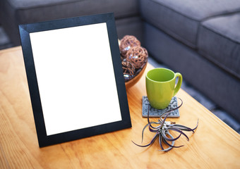 Blank picture frame on a coffee table with a green mug and decor in the living room.