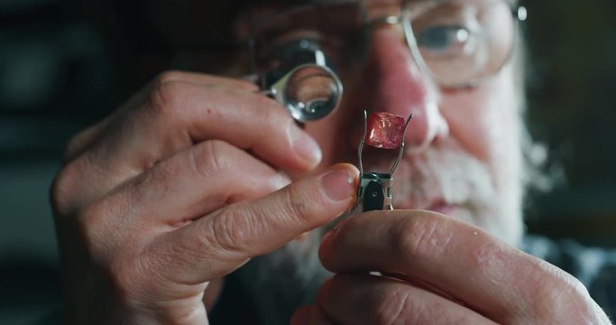 Slow motion close up of experienced goldsmith controlling a quality of precious gem, selected for making jewels in workshop