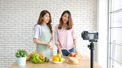 Two young asian women food bloggers talking while recording video with happy moment, vlog concept, people and technology communication