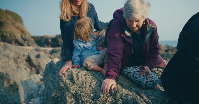 Little toddler sitting on a rock with his mother and grandparents