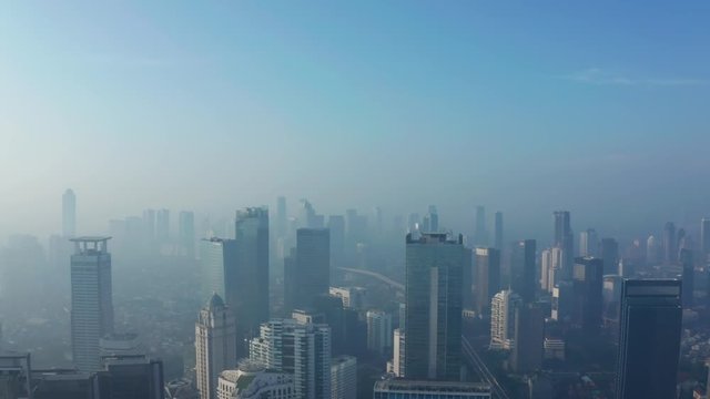 JAKARTA, Indonesia - April 25, 2019: Aerial landscape of Jakarta downtown with silhouette of skyscrapers behind fog of air pollution. Shot in 4k resolution from a drone flying from left to right
