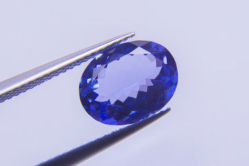 Big blue gemstone Placed on the wooden floor.blue sapphire oval stone in tweezer