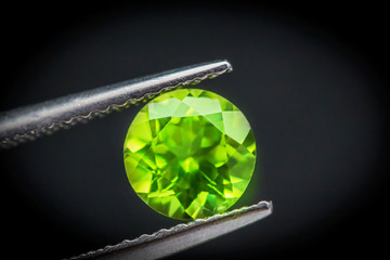 Peridot gemstone.Beautiful round shape gem.Natural Green Sapphire.stone in tweezers.Focus on the center of the image.The background is not smooth.