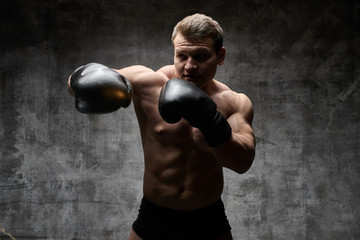 Naklejka na ściany i meble Muscular pumped man boxing in gloves on a black background. Sexy athletic body