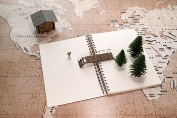  one traveler miniature walking to bridge with pine tree and one house on world map