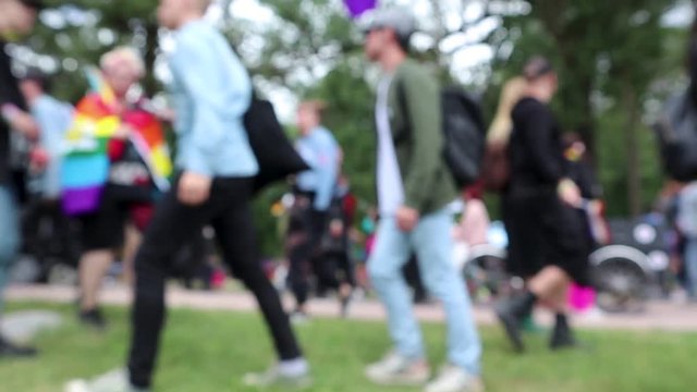 Defocused footage of a crowd at the park during LGBT pride parade. People with rainbow flags and balloons.