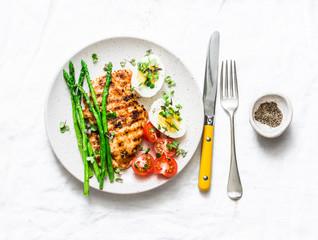 Grilled chicken steak, asparagus, boiled egg, cherry tomatoes - healthy diet lunch on a light background,  top view