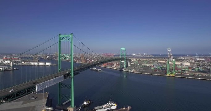 Aerial, rising, drone shot, parallel to the Vincent Thomas Bridge, overlooking traffic on seaside freeway 47 and the Terminal island, on a sunny day, in San Pedro, Los Angeles, California, USA