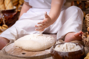 Obraz na płótnie Canvas a small child sits on a wooden table and rolls out the dough with a rolling pin,flour is scattered around and bread lies. the child develops fine motoriku gets skills