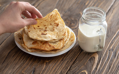 a man is having Breakfast, a mug of milk and a plate of fried corn tortillas on a wooden textured table looking over his shoulder. free text copy space