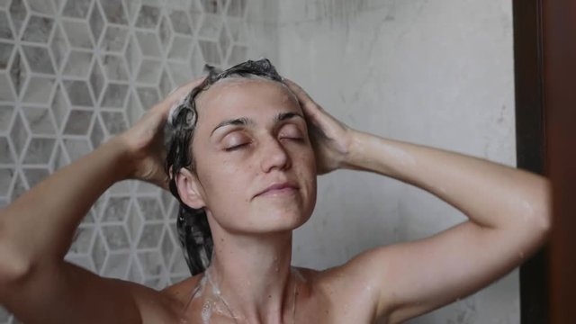 Portrait of young woman is washing her hairs with shampoo taking a shower with close eyes.