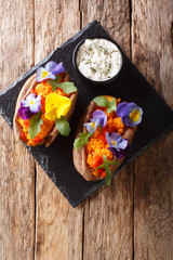 Organic baked sweet potato with edible flowers is served with sauce on the board. Vertical top view
