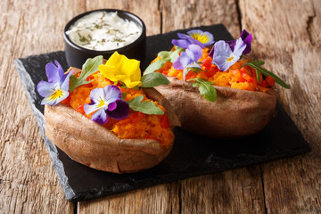 portion of baked yam with edible viola flowers is served with a sauce on the board. horizontal