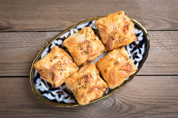 samosa with potatoes, meat and pumpkin on plate with traditional Uzbek ornament on wooden background, cooked in the tandoor. National Uzbek pastries. Flat lay.Top view. Street fast food. Rustic style