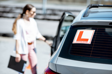 Learning sign on the car with woman driver on the background at the driving school outdoors