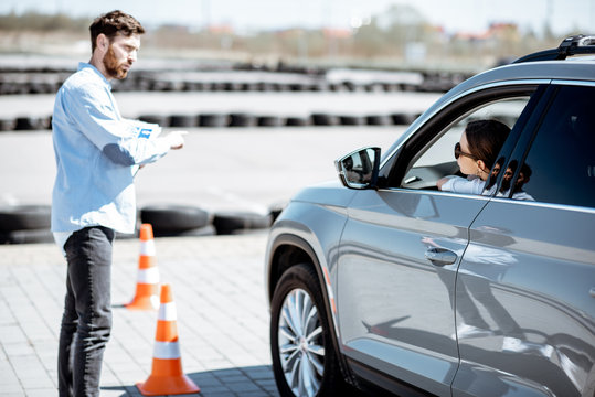 Male instructor teaching young woman driver to park a car on the training ground with traffic cones at the school