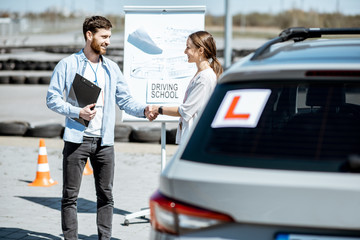 Male instructor shaking hand with a young female student on the training ground at the driver's school