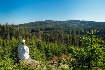Fototapeta na wymiar Young man sit on rock with forest and blue sky, looking to valley