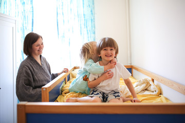 Siblings hugs with their mother on children's bed