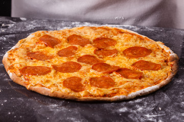 young woman in a gray aprong prepares a pepperoni pizza
