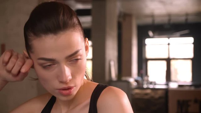 Closeup shoot of young attractive athlete female with ponytail working out on the orbitrek looking at camera and sweating in the gym indoors