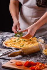 young woman in a gray aprong prepares a vegetarian pizza