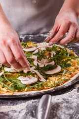 young woman in a gray aprong prepares a vegetarian pizza