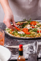 young woman in a gray aprong prepares a vegetarian pizza