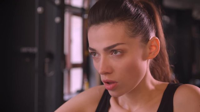 Closeup shoot of young attractive athlete healthy female with ponytail working out on the orbitrek looking at camera in the gym