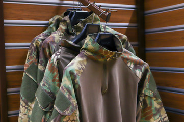 Camouflage clothes hanging on hangers in the room. a large number of military vehicles in the store