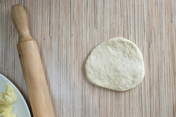 Yeast dough on the kitchen table is rolled out with a rolling pin for making a pie with a filling A cake of raw dough lies on the surface of the table for further preparation 