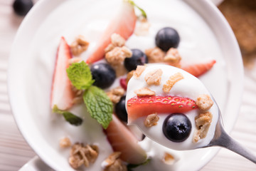 Top view of plain yogurt with fresh fruits and granola on top in spoon and  bowl on the table