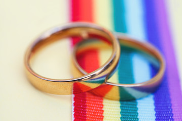 pair of golden wedding rings on LGBT rainbow ribbon on yellow background