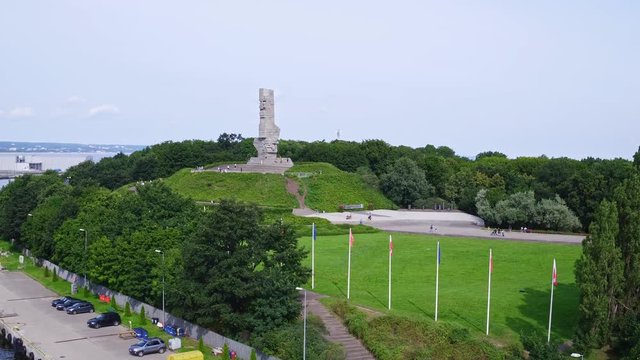Drone footage focus on Westerplatte Monument on a peninsula in Gdańsk harbor channel.