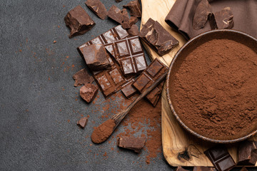 Dark Chocolate chunks and cocoa powder in wooden bowl on dark concrete background