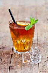 Traditional iced tea with lemon, mint leaves and ice cubes in glass on rustic wooden table.