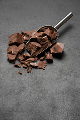 Dark Chocolate chunks in metal scoop on dark concrete background