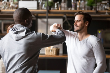African and caucasian buddies greeting each other with fist bumping