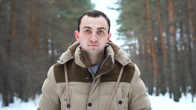 Portrait of a young man in a jacket in the forest. Man stands in winter forest