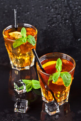 Two glasses with cold traditional iced tea with lemon, mint leaves and ice cubes.