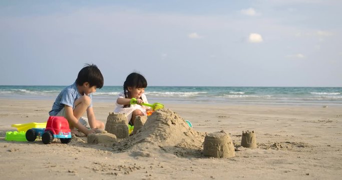 Little girl and her brother playing on the beach building sand castle together. Slow motion. Family, Holiday and Travel concept.