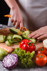 young woman in a gray apron cuts a cucumber