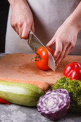young woman slicing a tomato in a gray apron