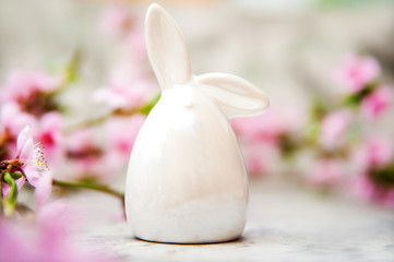 Spring blossom concept. Easter concept, miniature bunny, flowering tree close-up and copy space. Pink natural texture of natural flowering tree. Easter bunny and branches of blossoming on an table.
