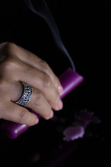 A woman's hand with a beautiful silver ring holds a smoking purple candle