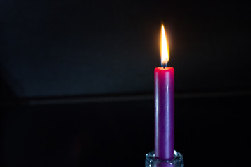 A lit purple candle with dark background