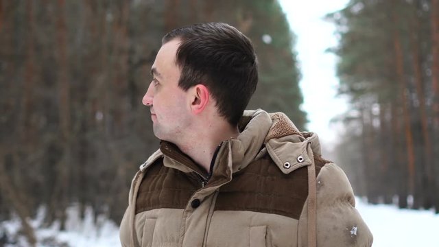 Portrait of young man in jacket is looking aside. Man stands in winter forest