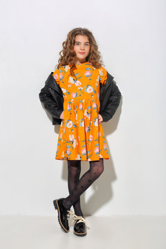 Fashion girl 10 years old in black leather jacket, yellow dress posing in the Studio. Curly hair, black shoes.