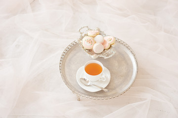 Silver tray with a cup of tea and macarons on a wooden white table in a white room